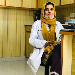 Female Dentist, Doctor Kiran Haseeb wearing a white lab coat and sitting on a chair in a dental clinic in Islamabad