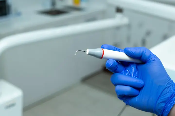 Ultrasonic scaler held in a gloved hand, ready for scaling and polishing